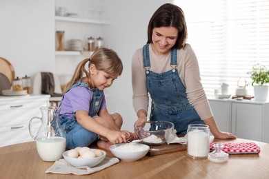 Photo of Little girl helping her mom making dough at table in kitchen