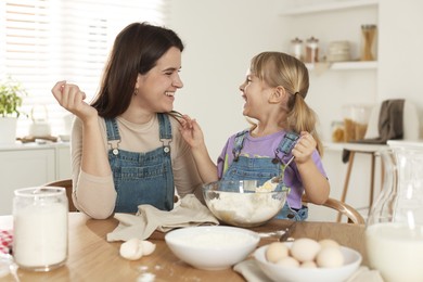 Little girl helping her mom making dough at table in kitchen