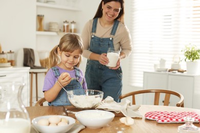 Photo of Little girl helping her mom making dough at table in kitchen