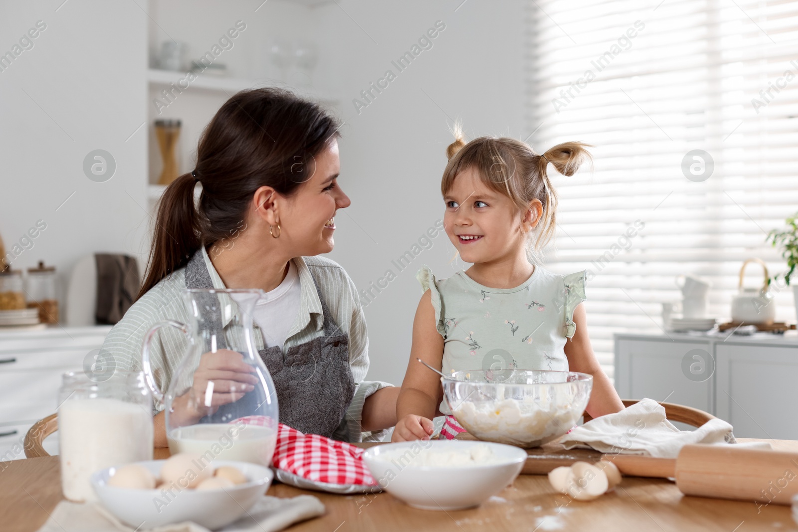 Photo of Little girl helping her mom making dough at table in kitchen