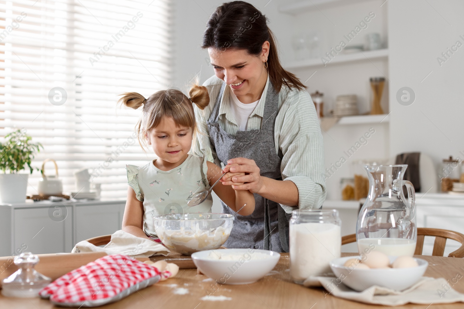 Photo of Little girl helping her mom making dough at table in kitchen