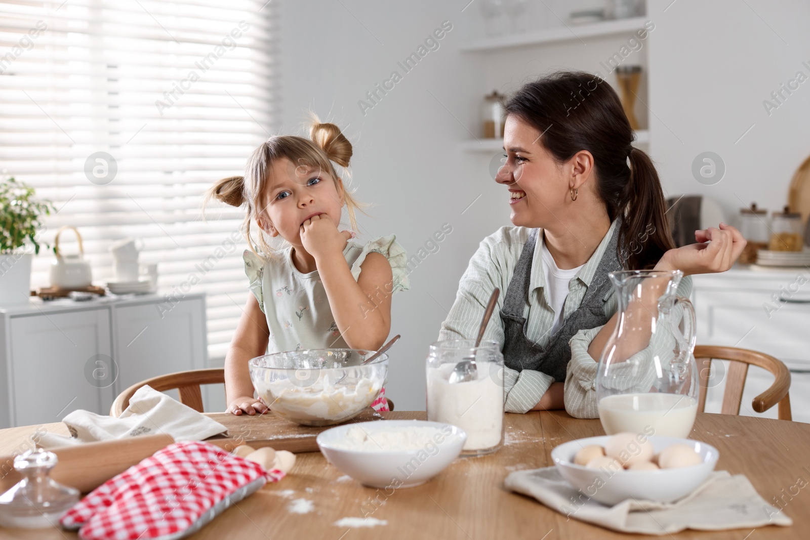 Photo of Little girl helping her mom making dough at table in kitchen