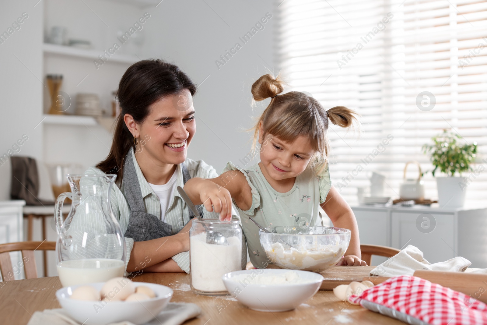 Photo of Little girl helping her mom making dough at table in kitchen