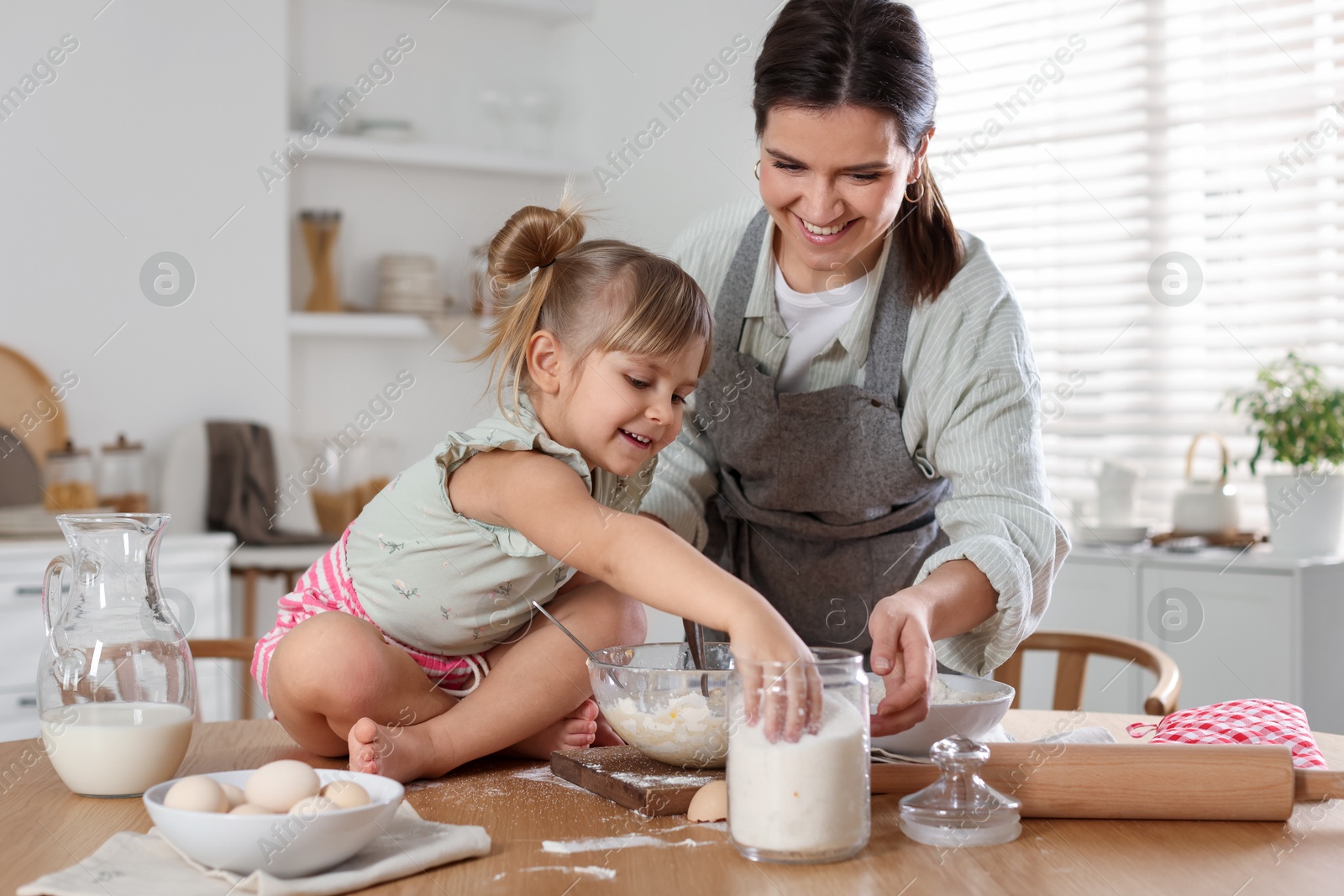 Photo of Little girl helping her mom making dough at table in kitchen