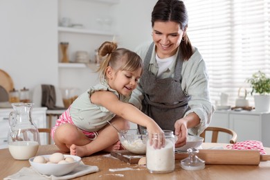 Little girl helping her mom making dough at table in kitchen