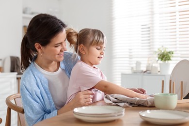 Photo of Little girl helping her mom wiping plates at table in kitchen