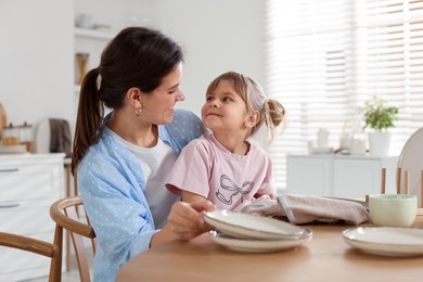 Photo of Little girl helping her mom wiping plates at table in kitchen