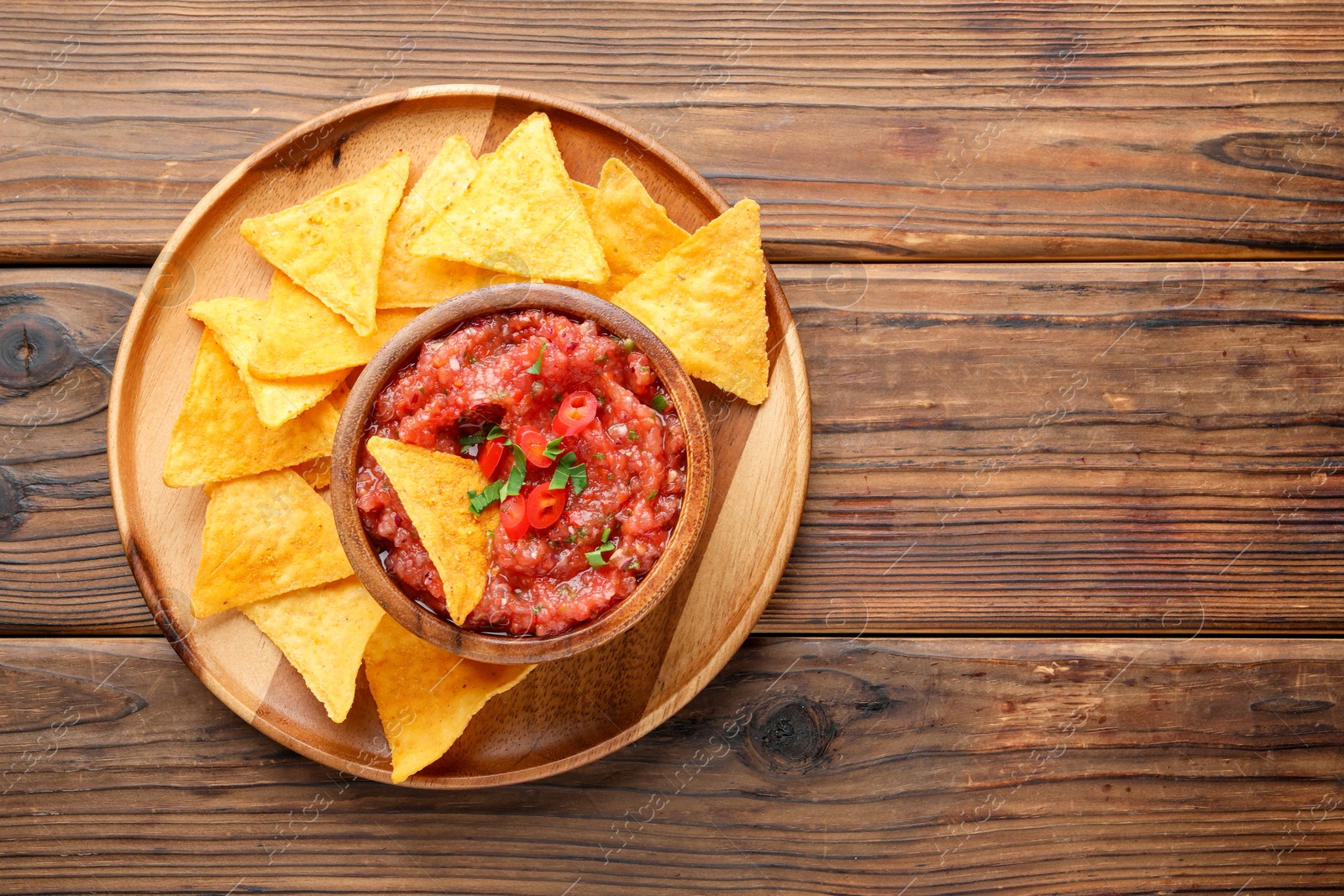 Photo of Delicious spicy salsa sauce in bowl and nacho chips on wooden table, top view. Space for text