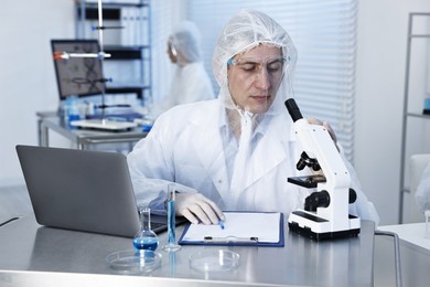 Scientist with laptop and microscope working at table in laboratory