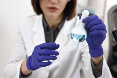 Photo of Scientist holding flask with sample in laboratory, closeup