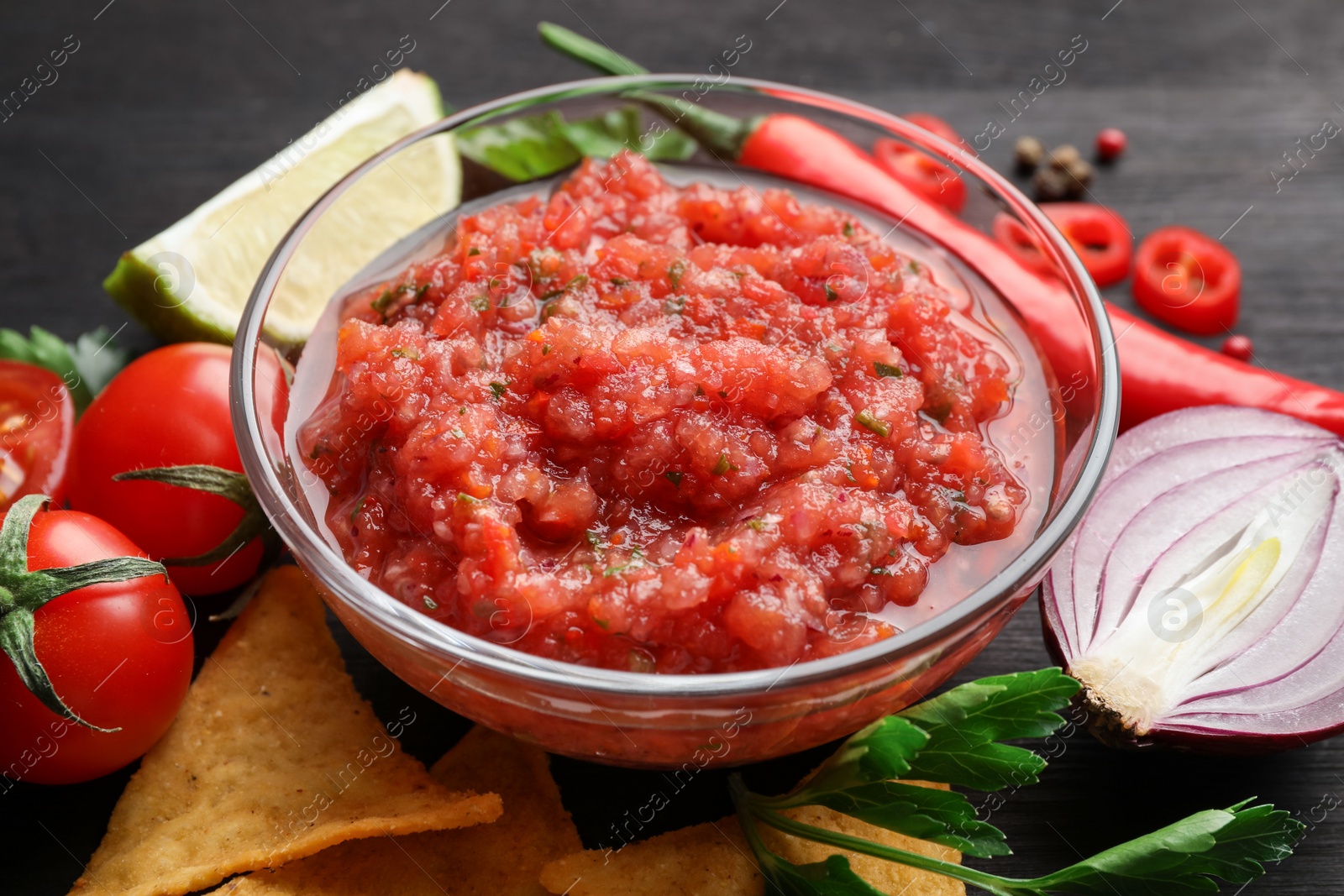 Photo of Spicy salsa sauce in bowl, nachos and ingredients on table, closeup