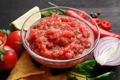 Photo of Spicy salsa sauce in bowl, nachos and ingredients on table, closeup