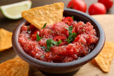 Photo of Spicy salsa sauce in bowl and nachos on table, closeup