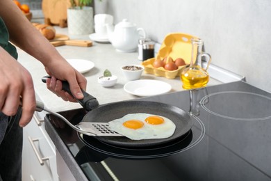 Man taking fried eggs from frying pan in kitchen, closeup