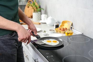 Man taking fried eggs from frying pan in kitchen, closeup