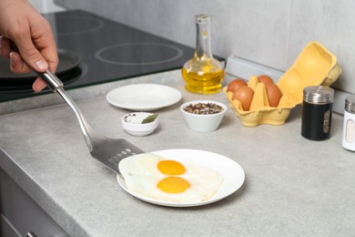 Photo of Man with frying pan putting tasty fried eggs onto plate in kitchen, closeup