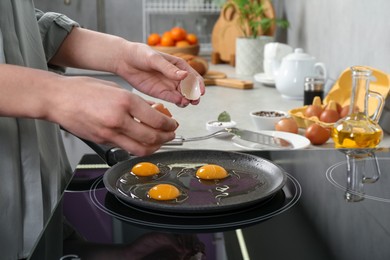 Woman breaking egg into frying pan in kitchen, closeup