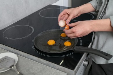 Photo of Woman breaking egg into frying pan in kitchen, closeup