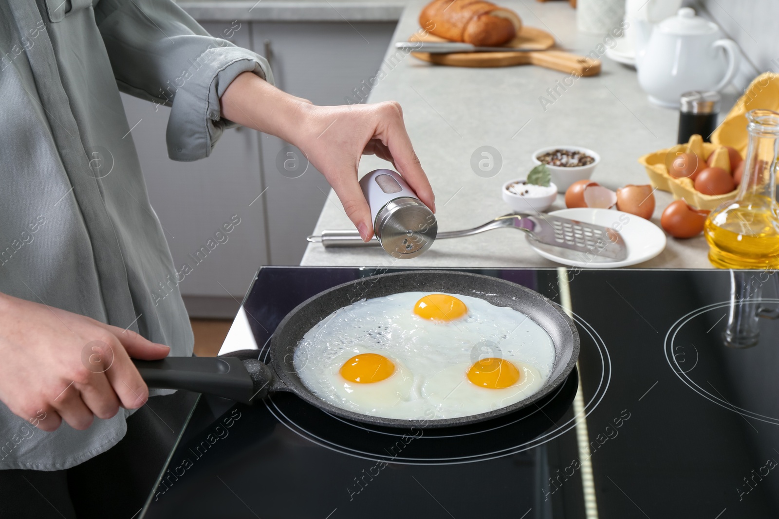 Photo of Woman adding salt into frying pan while cooking eggs on cooktop in kitchen, closeup