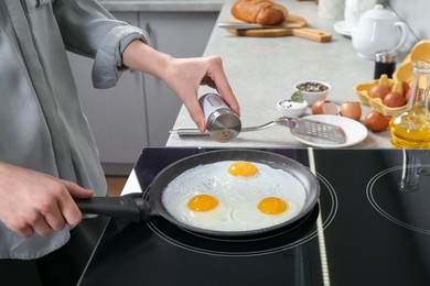 Woman adding salt into frying pan while cooking eggs on cooktop in kitchen, closeup