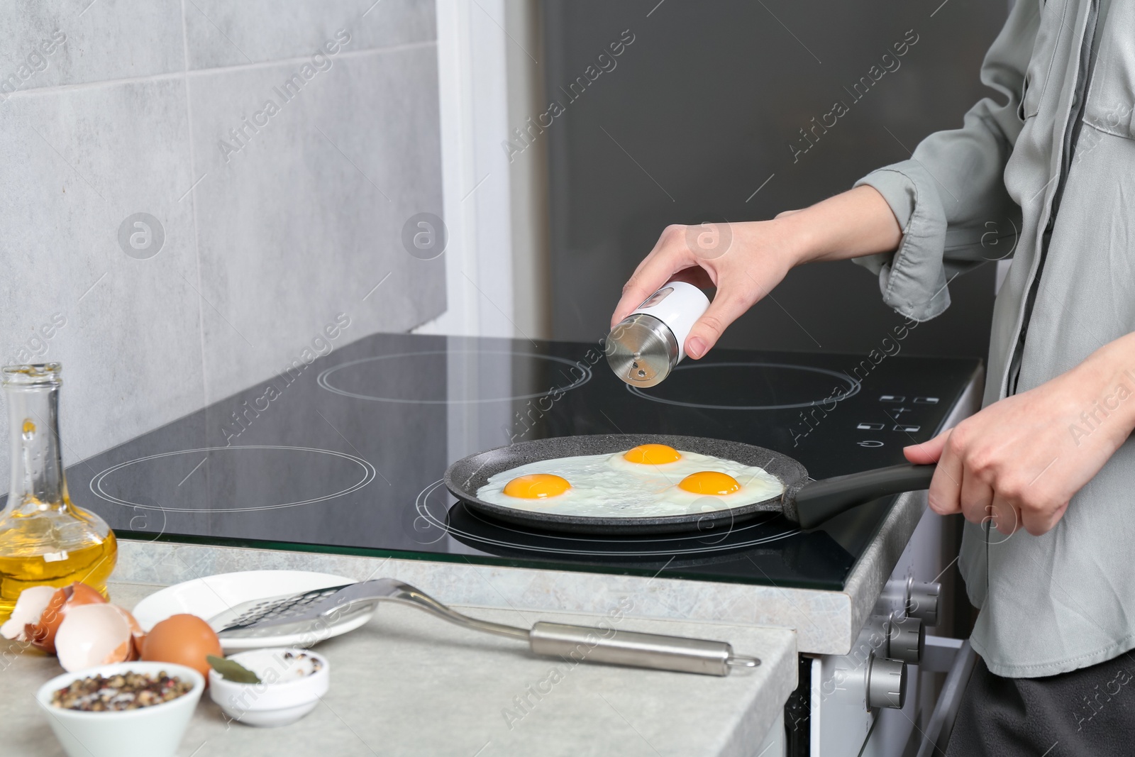 Photo of Woman adding salt into frying pan while cooking eggs on cooktop in kitchen, closeup