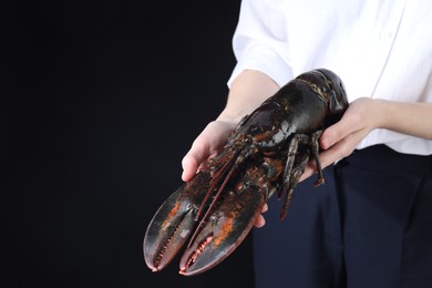 Photo of Woman with raw lobster on black background, closeup. Space for text