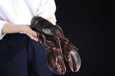 Woman with raw lobster on black background, closeup. Space for text