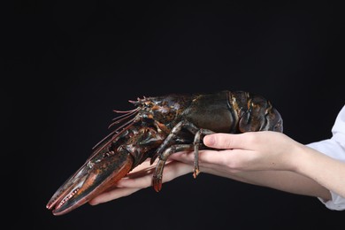 Woman with raw lobster on black background, closeup