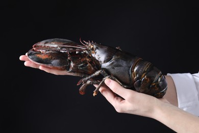 Photo of Woman with raw lobster on black background, closeup