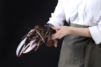 Photo of Woman with raw lobster on black background, closeup