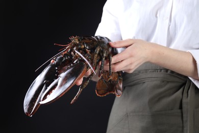 Woman with raw lobster on black background, closeup