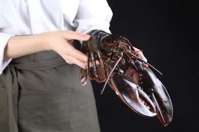 Photo of Woman with raw lobster on black background, closeup