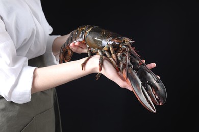 Photo of Woman with raw lobster on black background, closeup