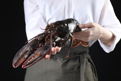 Woman with raw lobster on black background, closeup