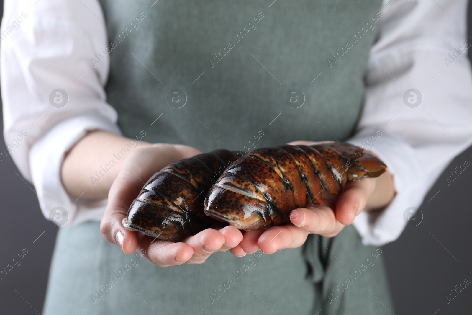 Photo of Woman with raw lobster tails on dark grey background, closeup