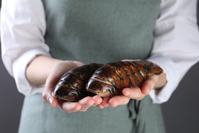 Woman with raw lobster tails on dark grey background, closeup