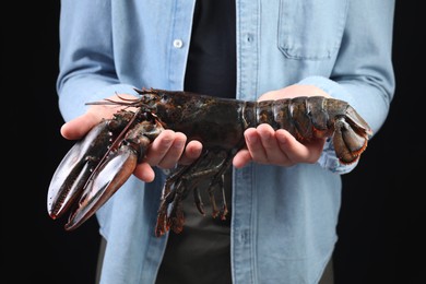 Photo of Man with raw lobster on black background, closeup