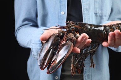 Man with raw lobster on black background, closeup