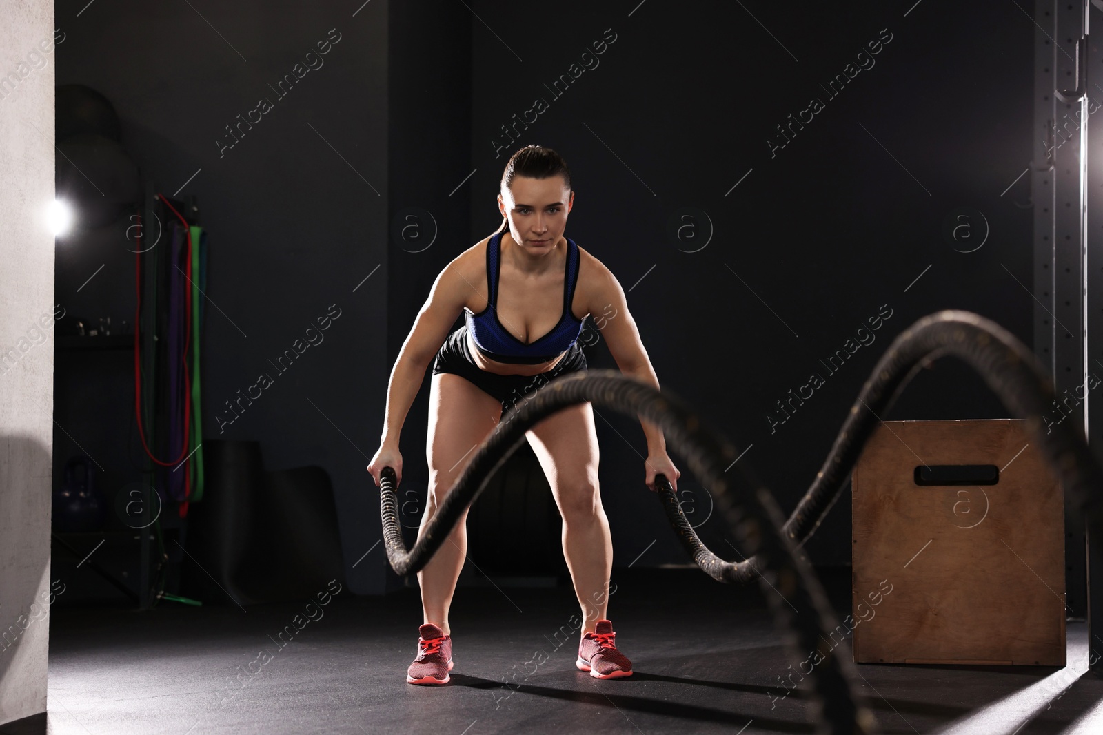 Photo of Sportswoman exercising with battle ropes during crossfit workout in gym