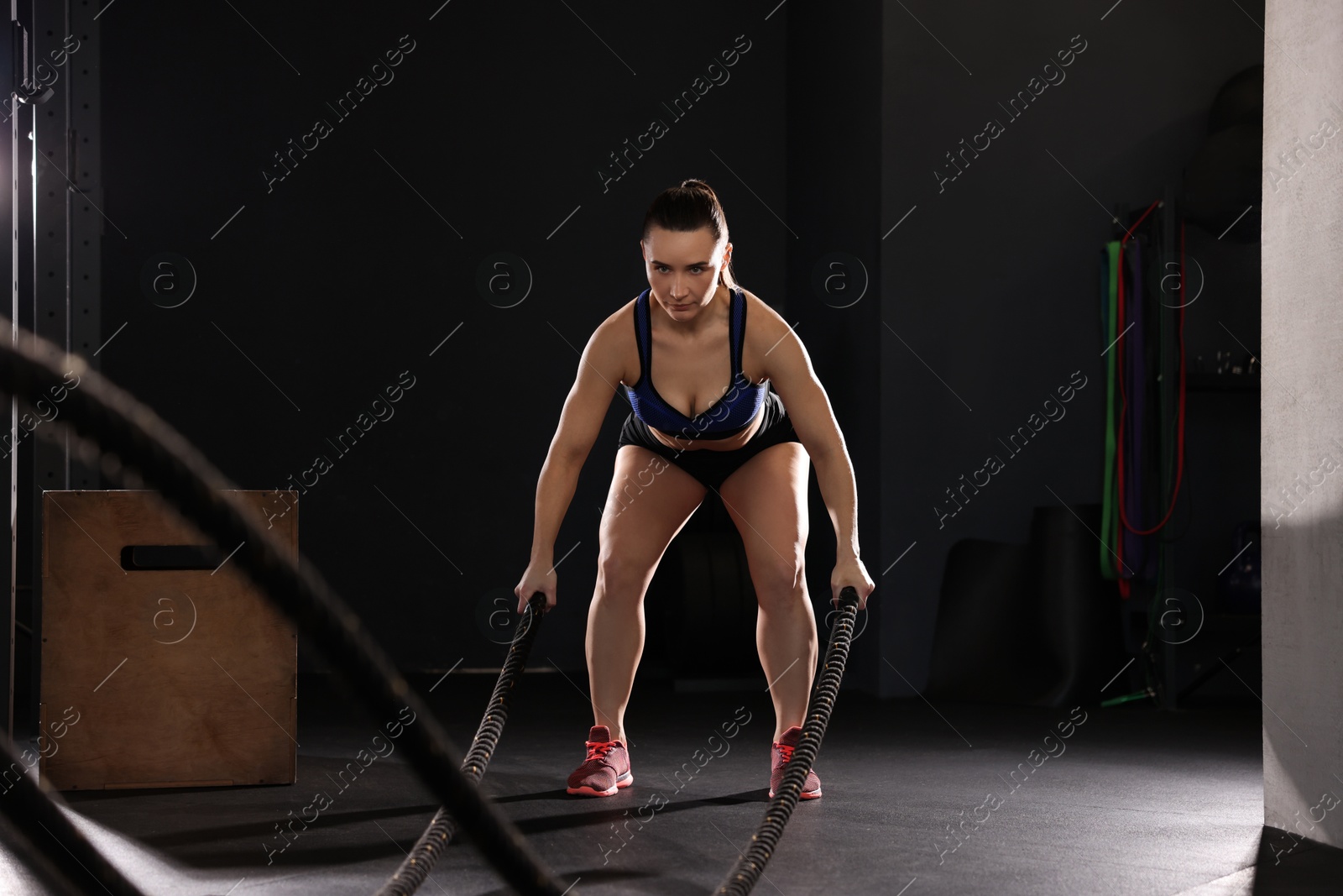 Photo of Sportswoman exercising with battle ropes during crossfit workout in gym