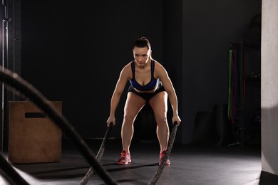 Photo of Sportswoman exercising with battle ropes during crossfit workout in gym