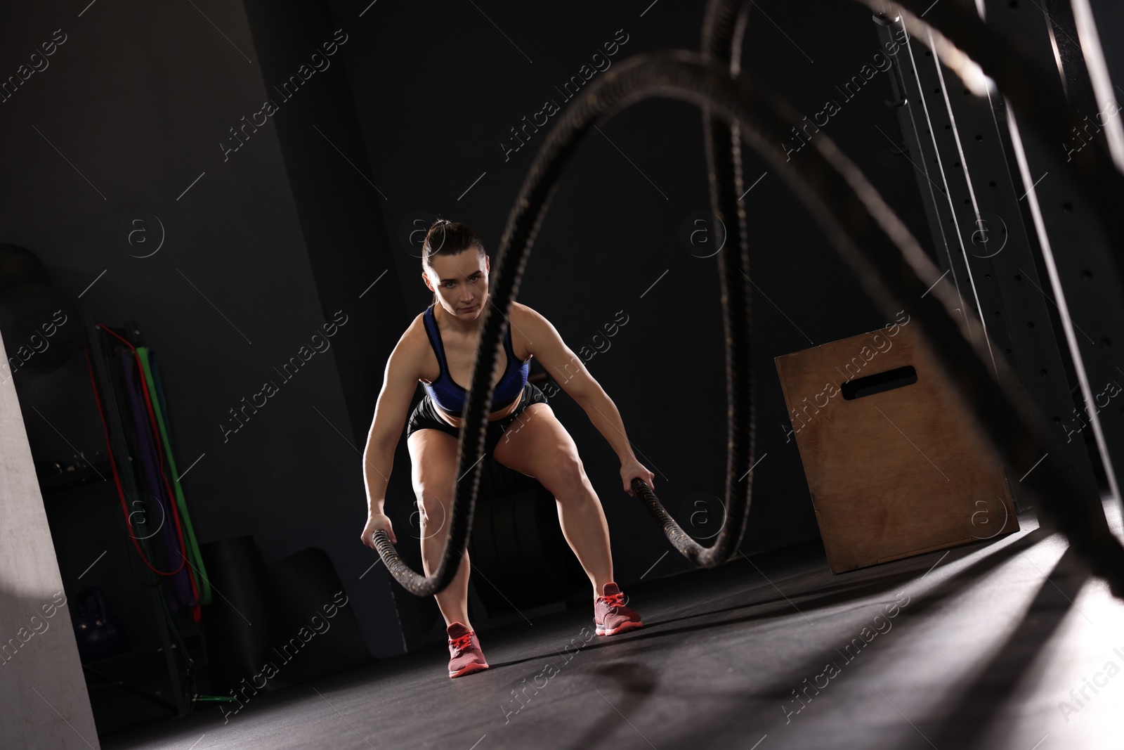 Photo of Sportswoman exercising with battle ropes during crossfit workout in gym