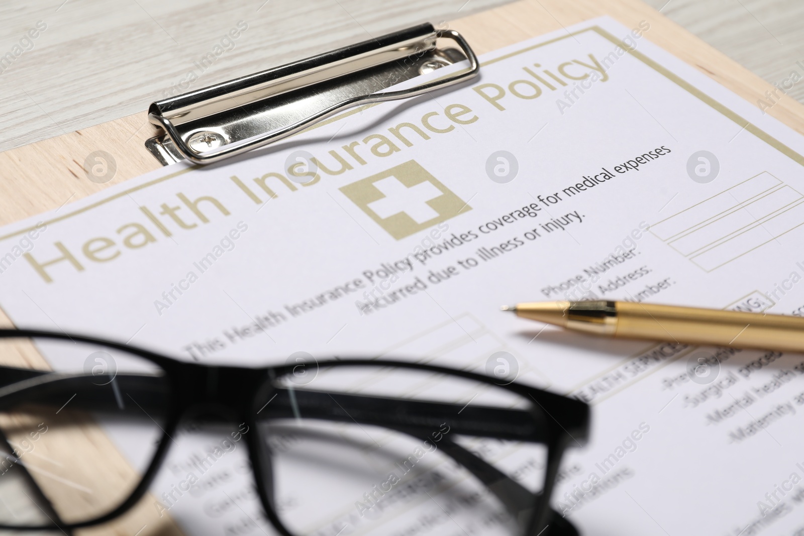 Photo of Health insurance policy form, glasses and pen on table, closeup