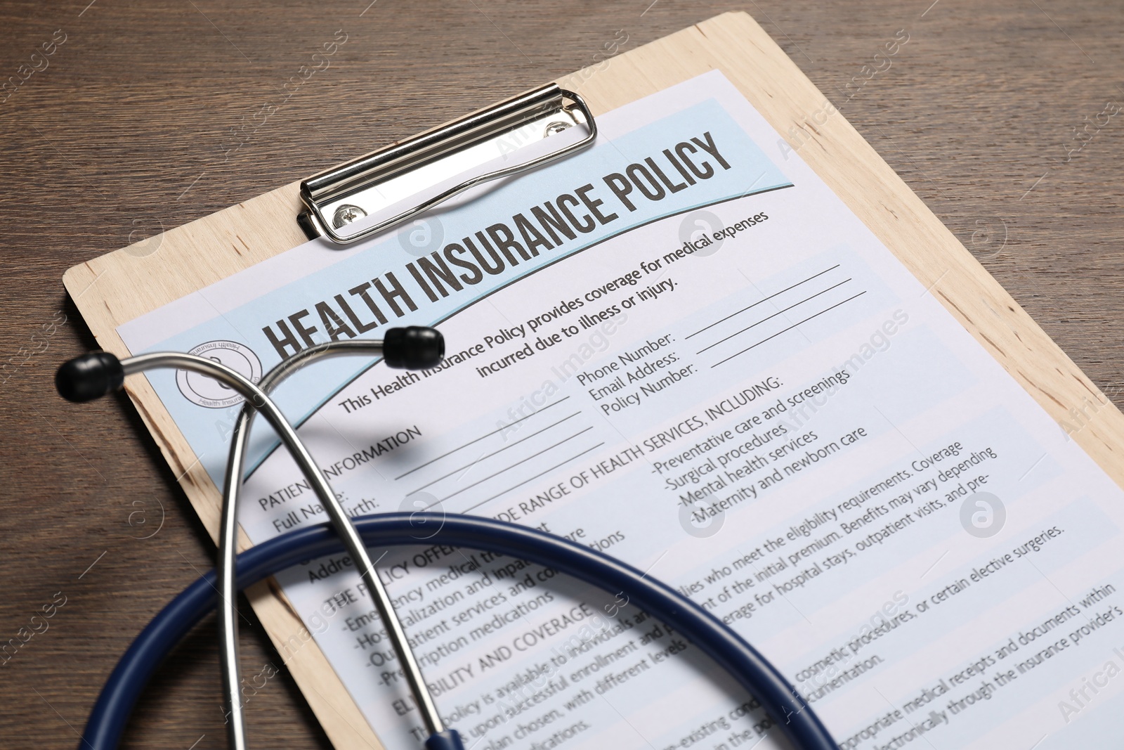 Photo of Health insurance policy form and stethoscope on wooden table, closeup