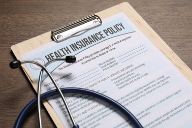 Health insurance policy form and stethoscope on wooden table, closeup