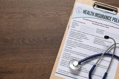 Photo of Health insurance policy form and stethoscope on wooden table, top view. Space for text