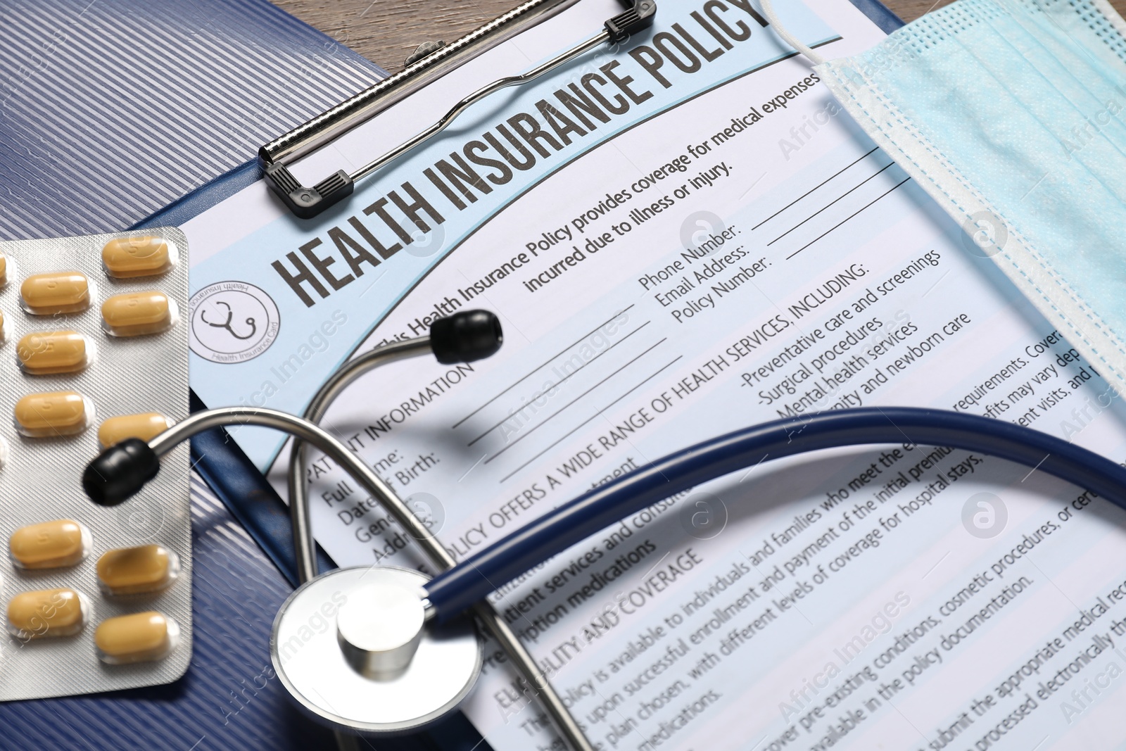 Photo of Health insurance policy form, stethoscope, medical mask and pills on table, closeup