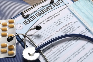 Health insurance policy form, stethoscope, medical mask and pills on table, closeup