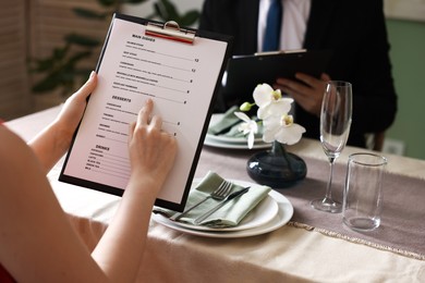 Photo of Couple choosing dishes from menu at table in restaurant, closeup