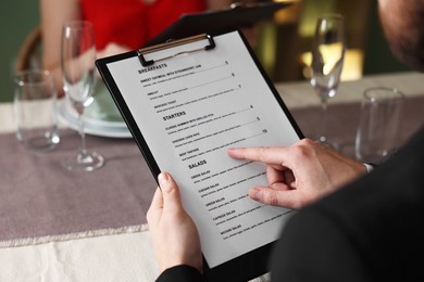 Couple choosing dishes from menu at table in restaurant, closeup